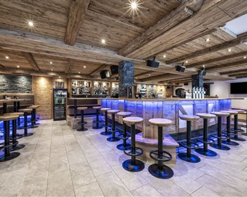 Eine moderne Bar mit Holzdekor und stimmungsvollem Licht. Die Sitzplätze sind um die zentrale Theke angeordnet.