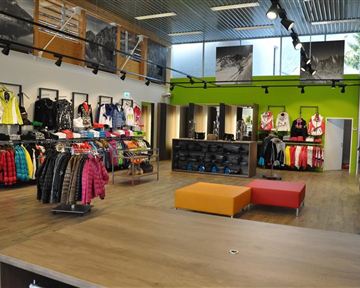 A modern sportswear store with colorful jackets and equipment. In the center, there are orange seats and the walls are decorated with pictures.