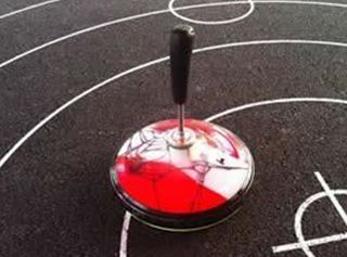 A colorful spinning top stands on a sports field with black lines. The ground has various field markings.