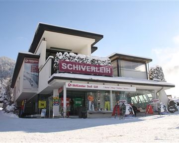 Ein modernes Geschäft für Skiverleih im verschneiten Winterlandschaft. Die Fassade zeigt große Fenster und ein einladendes Schild mit der Aufschrift "Schiverleih".