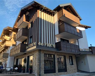 A modern building with wooden cladding and balconies. The façade is inviting and stylishly designed.