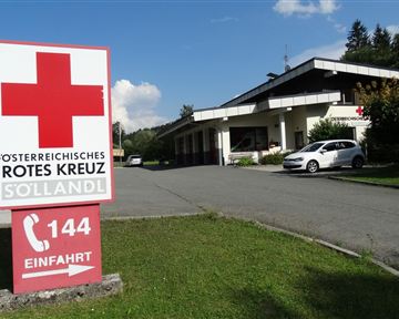 Ein Gebäude des Österreichischen Roten Kreuzes in Söllandl. Im Vordergrund steht ein großes, rotes Kreuz-Schild mit der Telefonnummer 144.
