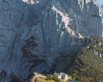 Eine beeindruckende Berglandschaft mit steilen Felsen und einer schönen Wiese im Vordergrund. Im Hintergrund erhebt sich majestätisch der Felsen.