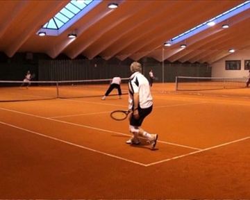 A tennis match in a hall with an orange floor covering. Several players are actively playing and focusing on the game.