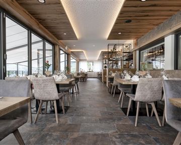 Ein modernes Restaurant mit hellem Ambiente und großen Fenstern. Holz- und Steinelemente schaffen eine einladende Atmosphäre.