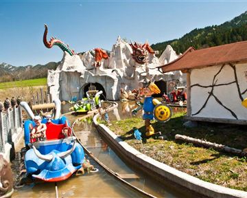 A theme park with a water ride and colorful figures. In the background, mountains and a blue sky can be seen.