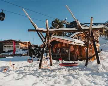 Zwei Personen in Winterkleidung stehen auf einer Eisbahn. Sie halten Besen und sitzen auf bunten Schlittenfiguren.