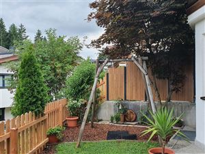 A beautiful garden with a wooden swing, green plants, and a wooden fence. The sky is cloudy and the atmosphere is calm.
