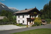 A beautiful two-story house with traditional architecture in a green landscape. In the background, there are mountains and a clear blue sky.