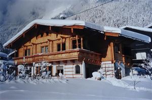 Ein charmantes Chalet im Schnee, umgeben von verschneiten Bäumen. Die Fassade ist aus Holz und verleiht dem Haus eine gemütliche Atmosphäre.