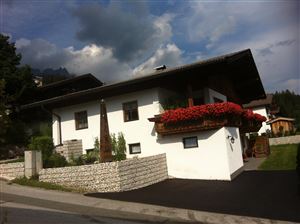 A beautiful, modern house with white walls and red flower boxes. In the background, there are green trees and a cloudy sky.