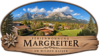 Eine malerische Landschaft mit Blick auf die Berge des Wilden Kaisers und einer charmanten Ferienwohnung. Grüne Wiesen und traditionelle Häuser prägen die Umgebung.