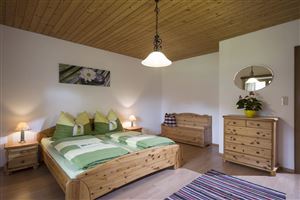 Ein gemütliches Schlafzimmer mit einem Doppelbett und Holzmöbeln. Es gibt eine schöne Beleuchtung und einen kleinen Spiegel an der Wand.