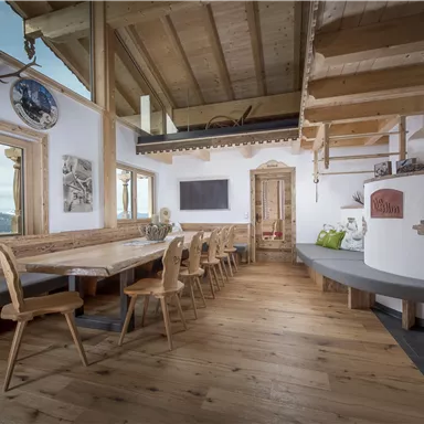 A cozy room with a large table and wooden chairs. The room has a rustic atmosphere and offers a beautiful view of the mountains.