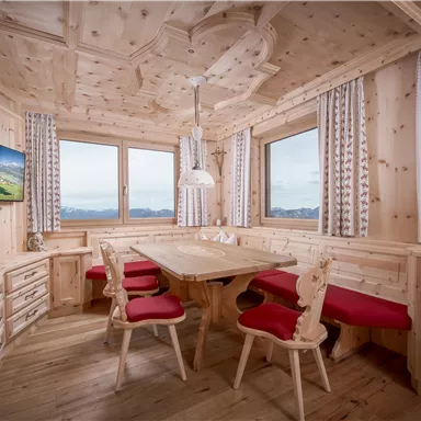 A cozy dining area made of light wood with red chairs. Large windows provide a view of the surrounding landscape.