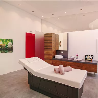 Ein modernes Wellnesszimmer mit einem Massagebett und Holzregalen. An den Wänden hängen Bilder von entspannenden Naturmotiven.