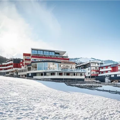 Ein modernes Gebäude in einem verschneiten Landschaft. Im Hintergrund erstrecken sich Wälder und eine vorbeigehende Bergkette.