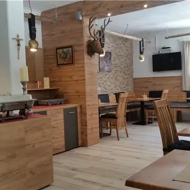 Ein gemütliches Restaurant mit Holzdekor und modernen Möbeln. Es gibt Tische mit Stühlen und eine einladende Atmosphäre.