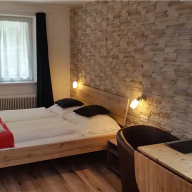 Ein modernes Schlafzimmer mit einem Doppelbett, einer Holzwand und einem Arbeitsplatz. Das Zimmer hat große Fenster und eine gemütliche Atmosphäre.