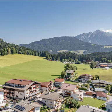 A picturesque village in a green landscape with a view of the mountains. The houses are surrounded by meadows and forests.