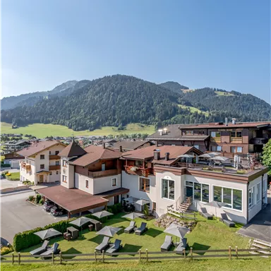 A beautiful hotel amidst a green landscape with mountains in the background. The terraces are equipped with loungers and invite relaxation.