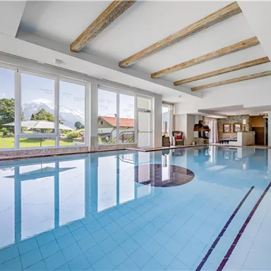 A stylish indoor pool with large windows and a view of the mountains. The water is clear and the architecture is modern and welcoming.
