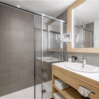 A modern bathroom with a glass shower and a wooden sink. The room is bright and clean with neutral colors.
