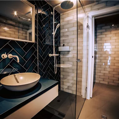 A modern bathroom with blue tiles and an elegant sink. The shower is separated by a glass wall and offers plenty of light.