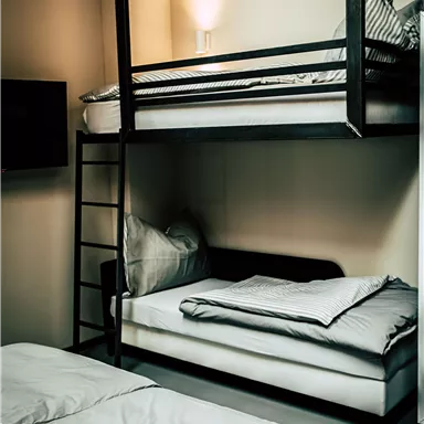 Ein modernes Schlafzimmer mit einem Etagenbett und einem Schlafsofa. Die Wände sind hell und die Beleuchtung ist warm.