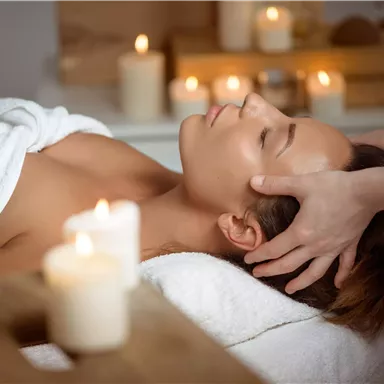 A relaxing wellness treatment with a woman receiving a head massage. The surroundings feature candles and a tranquil atmosphere.