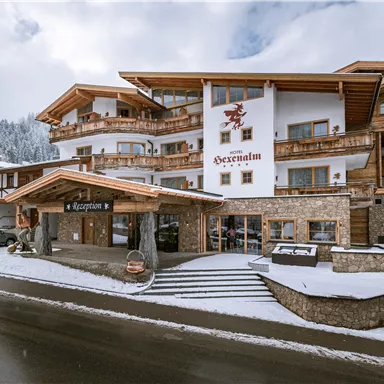 A charming hotel in alpine style, surrounded by snow-covered mountains. The facade is made of wood and stone, with a cozy entrance area.