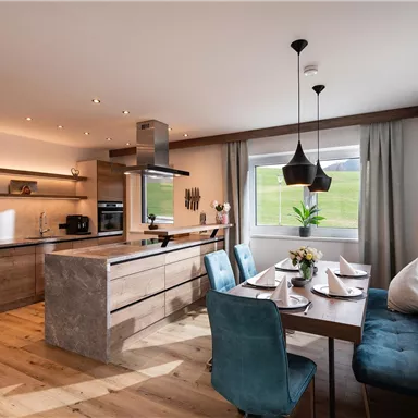 Moderne Küche mit Holzregalen und einem Essbereich. Der Raum ist hell und freundlich mit Pflanzen und eleganten Möbeln.