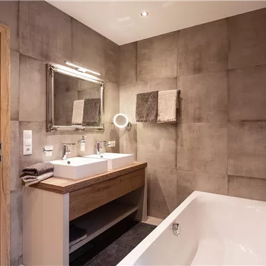 A modern bathroom with a freestanding bathtub and a double sink. The walls are designed in a concrete look, and a large mirror adds style.