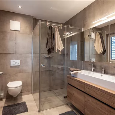 Ein modernes Badezimmer mit einer Glasdusche und Holzregalen. Der Raum ist schlicht und elegant gestaltet.