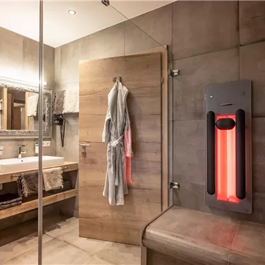 Ein modernes Bad mit Holz- und Betonelementen. Es gibt ein Waschbecken, einen Spiegel und eine Infrarotwärmelampe.