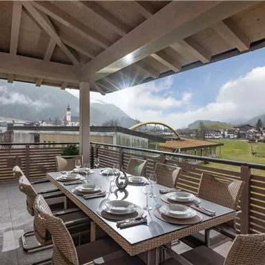 A spacious terrace with a large dining table and stylish chairs. In the background, there are mountains and a picturesque landscape.