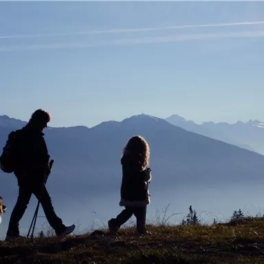 Eine Person, ein Kind und ein Hund wandern in den Bergen. Der Himmel ist klar und die Landschaft ist von Bergen umgeben.