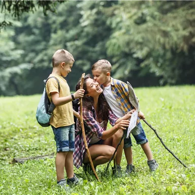 Eine Mutter verbringt Zeit mit ihren zwei Söhnen in der Natur. Sie lächeln und genießen die gemeinsame Zeit beim Wandern.
