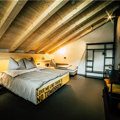 A modern designed bedroom with a wooden beam ceiling and two beds. The decor is simple and stylish, with a large window that provides plenty of light.