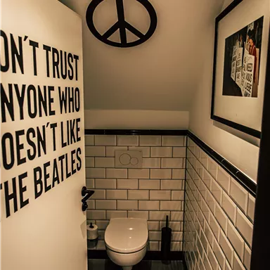 A modern bathroom with white tiles and a minimalist design. A sign on the wall alludes to the Beatles.