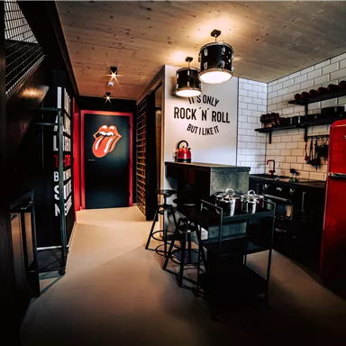 Eine stilvolle Küche mit einem roten Kühlschrank und einem modernen Esstisch. Die Wände sind kreativ gestaltet und verleihen dem Raum eine rockige Atmosphäre.