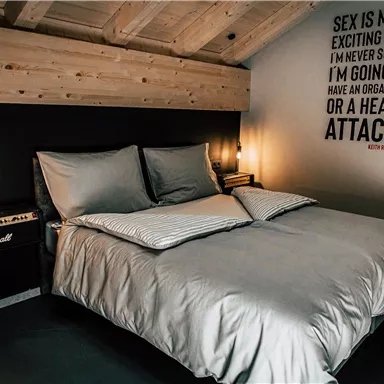 A modern bedroom with a large bed and a wooden ceiling. On the wall, there is a humorous saying that grabs attention.