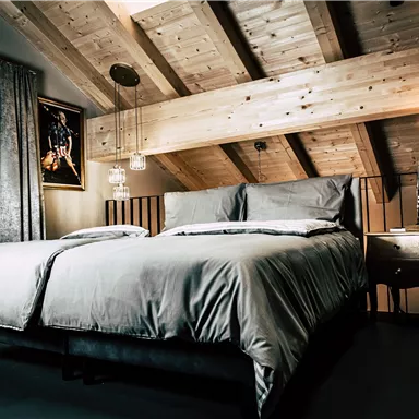 A modern bedroom with a large double bed and wooden ceilings. Daylight streams through a window, giving the room a cozy atmosphere.