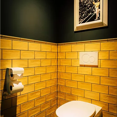 A modern bathroom with yellow tiles and an elegant toilet. A black and white picture hangs on the wall.