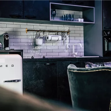 A modern kitchen with a white SMEG refrigerator and elegant black cabinets. The walls are tiled with shiny white tiles.