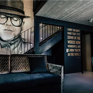 A modern interior with a large artwork on the wall depicting a portrait of a person. The room has a stylish decor and inspiring words on the wall.