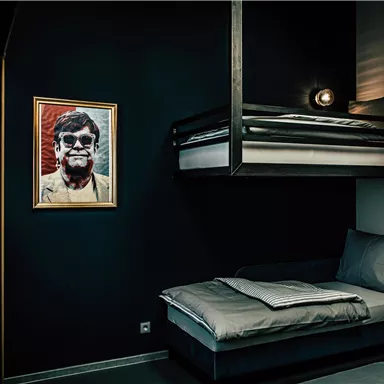 Ein modernes Zimmer mit einem Etagenbett und einem Einzelbett. An der Wand hängt ein gemaltes Porträt in einem goldenen Rahmen.