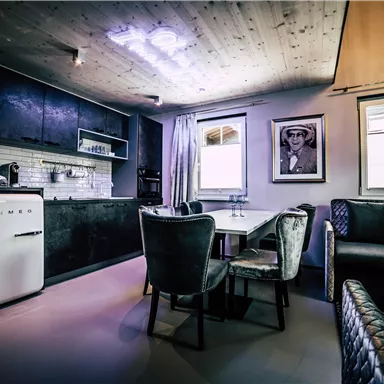 A modern kitchen with elegant furnishings and a cozy dining area. The walls are bright, and there are large windows that let in plenty of daylight.