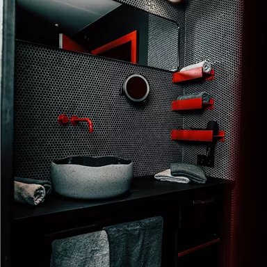A modern bathroom with a stylish sink unit and elegant decorations. The walls are in dark tones with red accents.