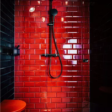 Eine moderne Dusche mit rotem Fliesenwand und schwarzem Duschkopf. Ein roter Hocker ergänzt das stilvolle Design.